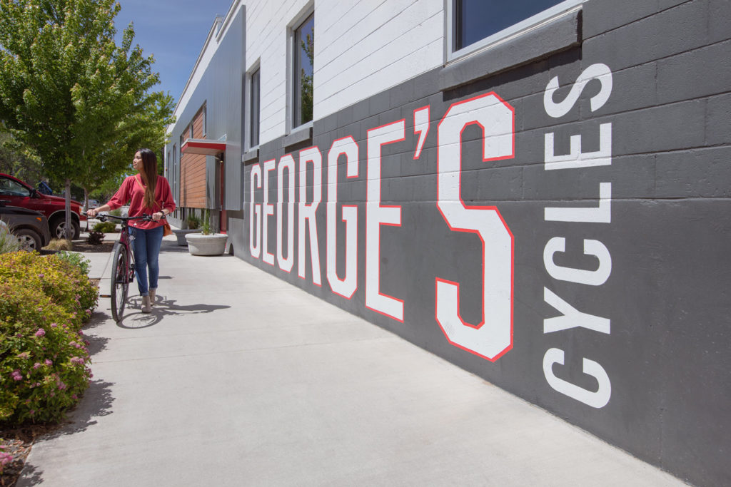 Young female walking with a bike past a sign reading George's Cycles