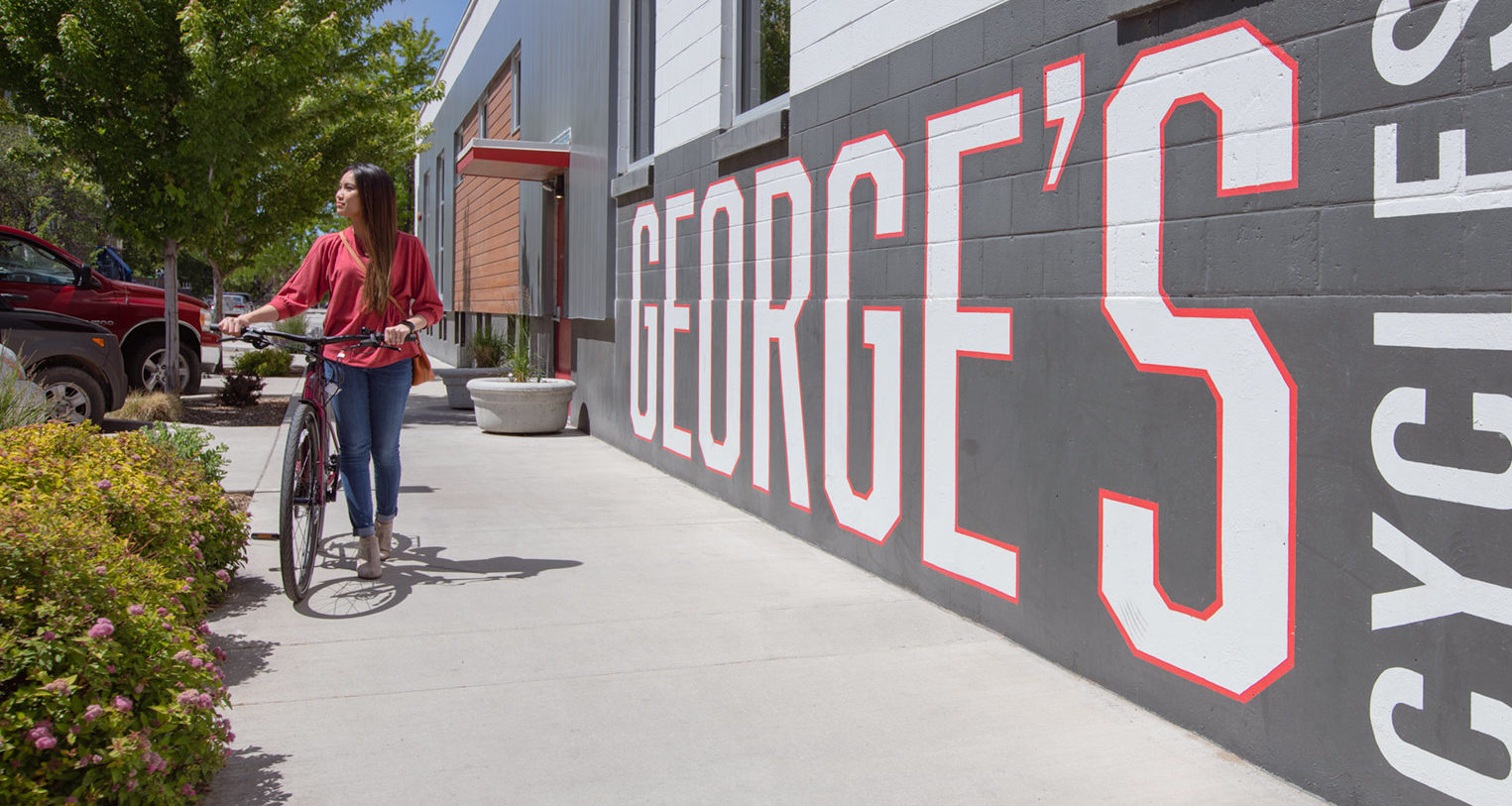 Young female walking with a bike past a sign reading George's Cycles